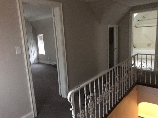 corridor with carpet floors, vaulted ceiling, and an upstairs landing