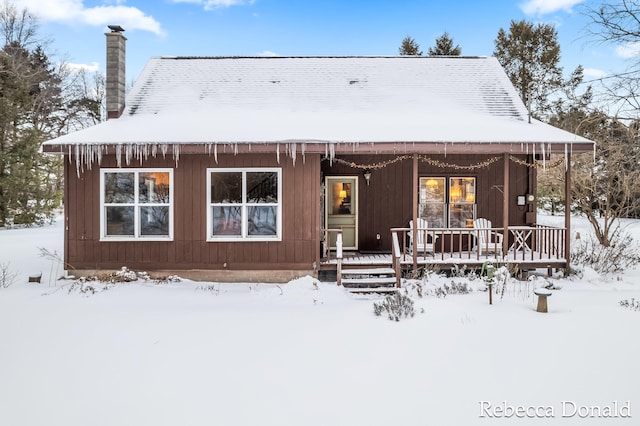 snow covered house with covered porch and a chimney