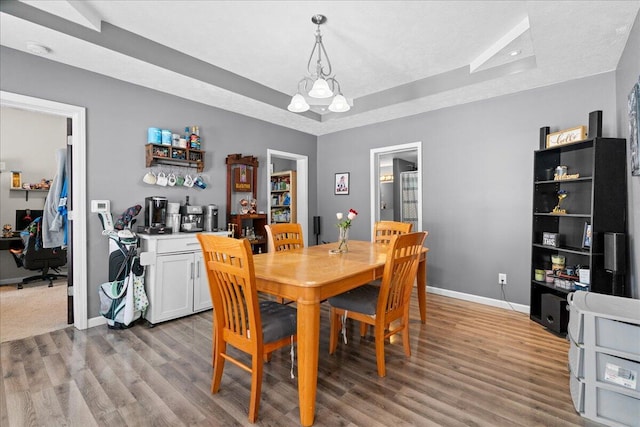 dining area featuring a notable chandelier, baseboards, a raised ceiling, and wood finished floors