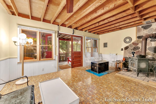 interior space featuring a sunroom, a wood stove, a wainscoted wall, and an inviting chandelier