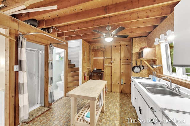 kitchen featuring ceiling fan, a sink, white cabinets, light countertops, and beamed ceiling