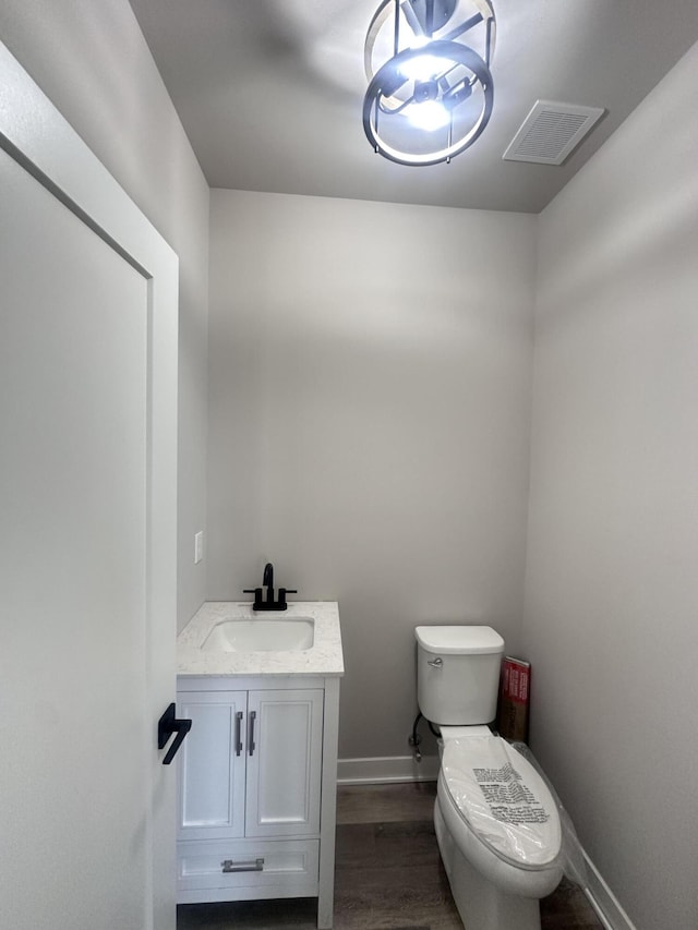 half bathroom featuring baseboards, visible vents, toilet, wood finished floors, and vanity