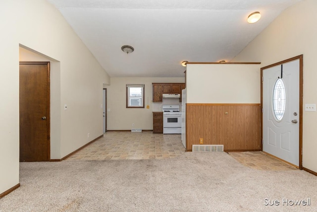 unfurnished living room featuring wooden walls, visible vents, light colored carpet, lofted ceiling, and a wainscoted wall