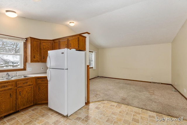 kitchen featuring brown cabinets, light countertops, light colored carpet, freestanding refrigerator, and a sink