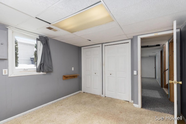 unfurnished bedroom featuring a paneled ceiling, visible vents, baseboards, carpet, and two closets