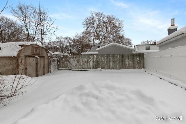 yard layered in snow with a fenced backyard, a storage unit, and an outbuilding