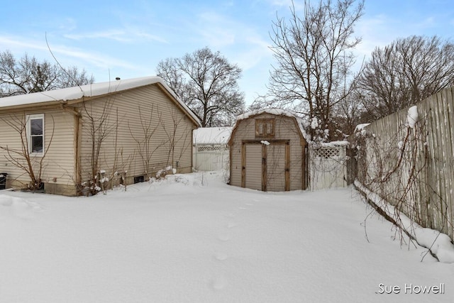 view of snow covered exterior featuring a shed, an outdoor structure, fence, and a gambrel roof