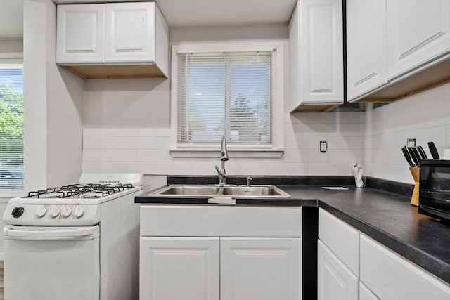 kitchen featuring white gas stove, dark countertops, backsplash, white cabinetry, and a sink