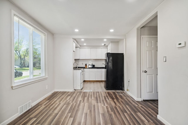 kitchen with visible vents, wood finished floors, freestanding refrigerator, white gas range, and white cabinetry