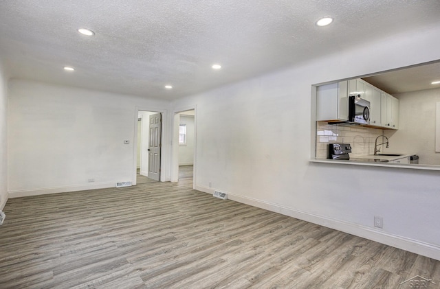 spare room with a textured ceiling, light wood-style flooring, recessed lighting, a sink, and baseboards