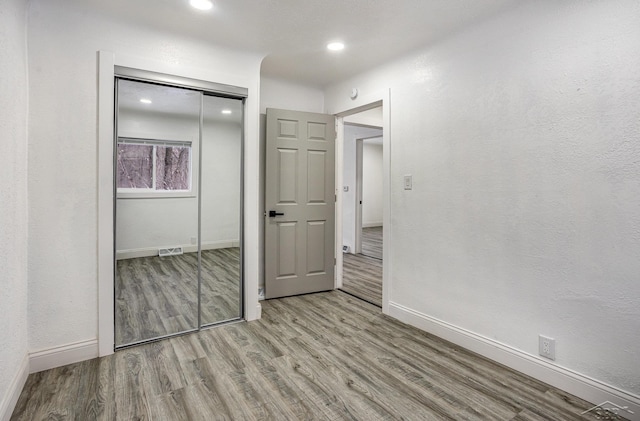 unfurnished bedroom featuring a textured wall, visible vents, baseboards, a closet, and light wood finished floors