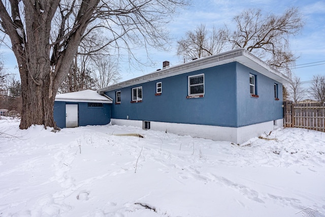 snow covered property featuring fence and stucco siding