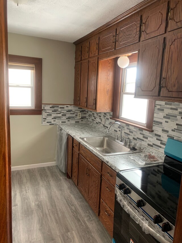 kitchen with electric range, a sink, decorative backsplash, light wood-style floors, and a textured ceiling