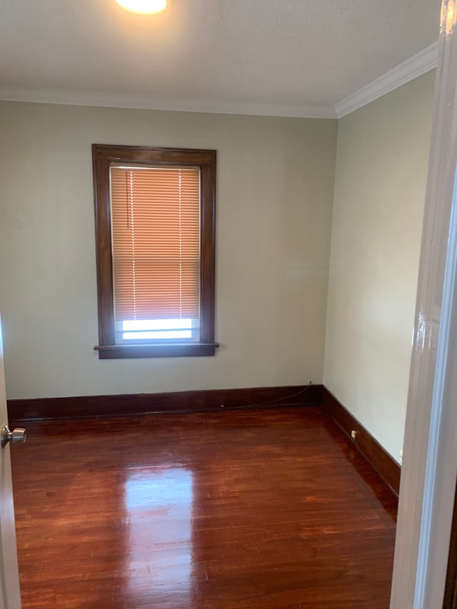 empty room featuring dark wood finished floors, ornamental molding, and baseboards