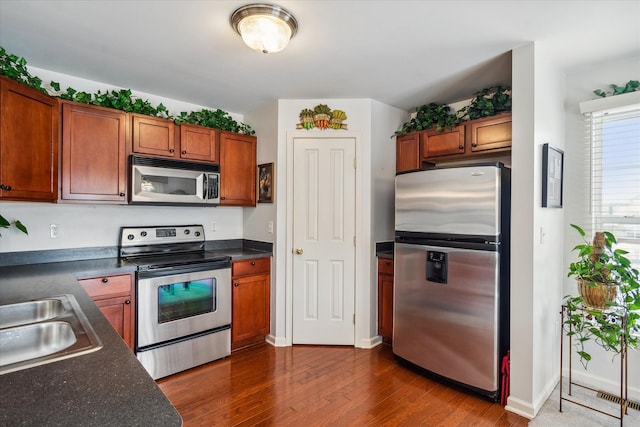 kitchen with dark countertops, brown cabinetry, stainless steel appliances, and dark wood-type flooring