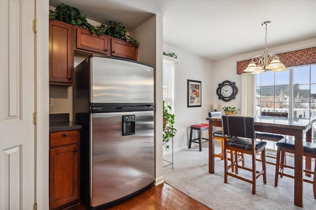 kitchen featuring stainless steel fridge, dark countertops, wood finished floors, hanging light fixtures, and a notable chandelier