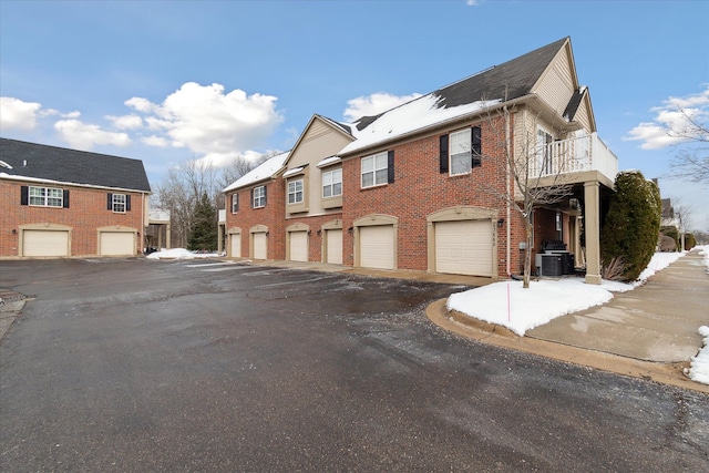 view of side of property featuring brick siding, central AC unit, and community garages