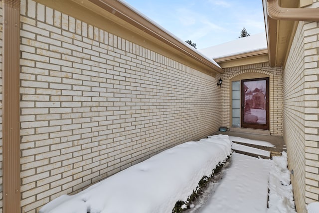 snow covered property entrance featuring brick siding