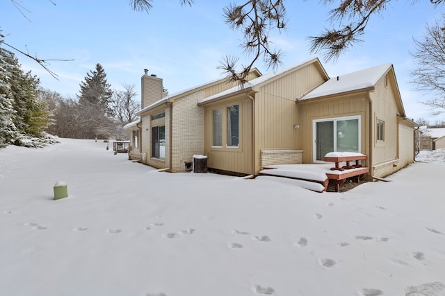 snow covered rear of property with brick siding and a chimney