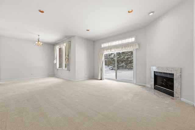 unfurnished living room featuring baseboards, a high end fireplace, light colored carpet, a chandelier, and recessed lighting