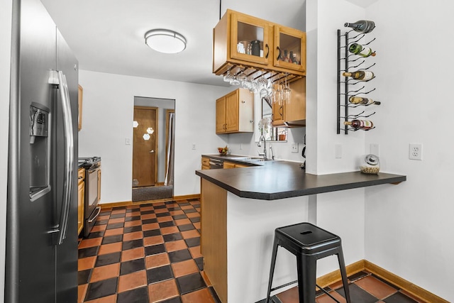 kitchen with stainless steel fridge, range with gas stovetop, dark countertops, glass insert cabinets, and a breakfast bar area