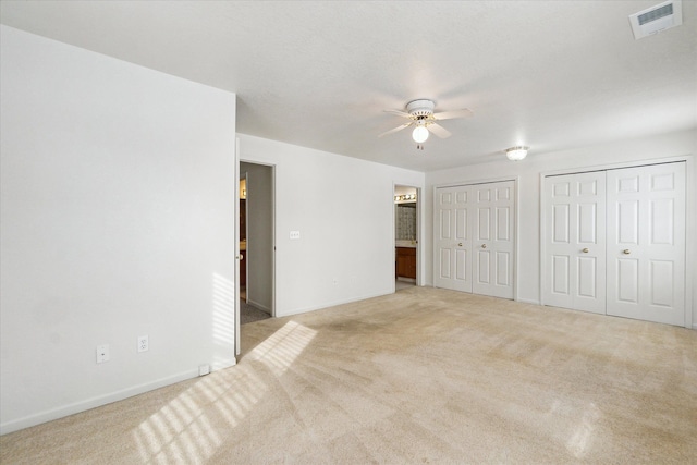 unfurnished bedroom featuring multiple closets, visible vents, light carpet, ensuite bath, and baseboards