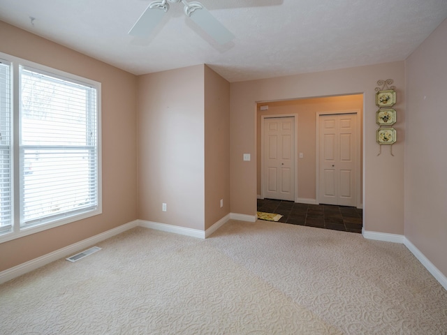 unfurnished room featuring dark colored carpet, visible vents, ceiling fan, and baseboards