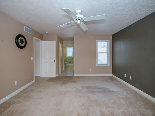 empty room with baseboards, visible vents, light carpet, and a textured ceiling