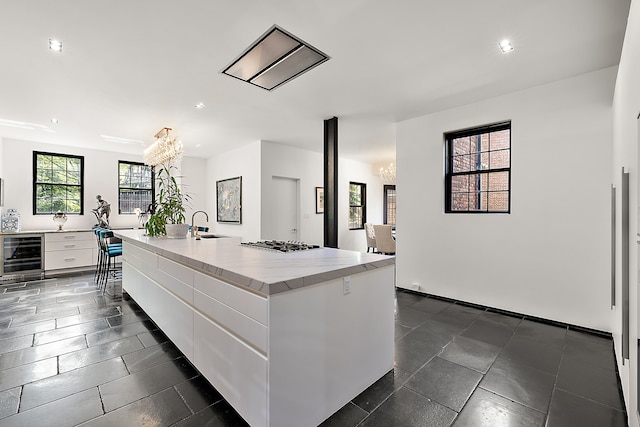 1771 Balmoral Dr, Detroit, MI 48203 - kitchen featuring wine cooler, an inviting chandelier, stainless steel gas stovetop, white cabinets, and a kitchen island with sink