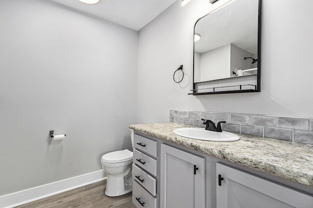 bathroom featuring toilet, wood finished floors, vanity, baseboards, and backsplash