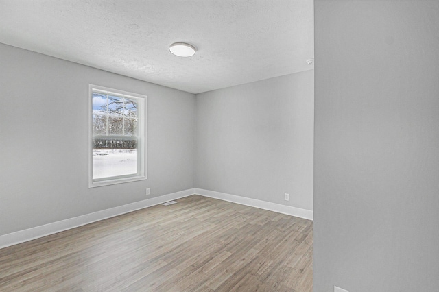 spare room featuring light wood-style floors, visible vents, a textured ceiling, and baseboards