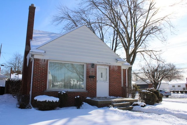 bungalow-style house with a chimney and brick siding