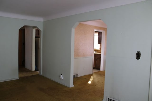 unfurnished room with carpet floors, arched walkways, and visible vents