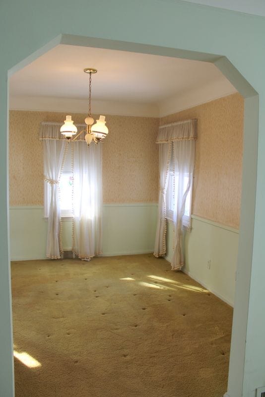 carpeted spare room with a notable chandelier, wallpapered walls, plenty of natural light, and a wainscoted wall