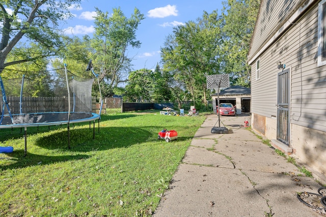 view of yard featuring a trampoline, a detached garage, and fence