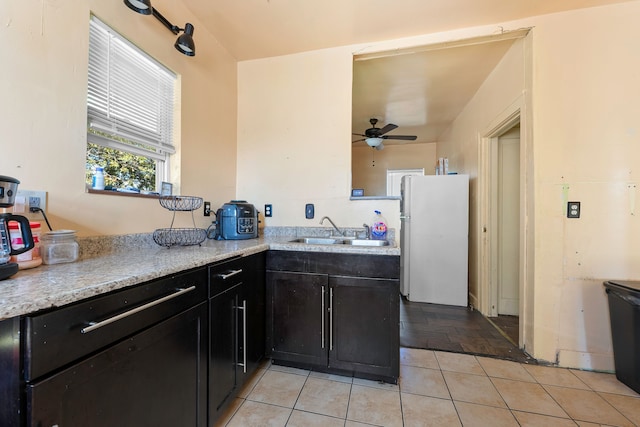 kitchen with freestanding refrigerator, a sink, a peninsula, and light stone countertops