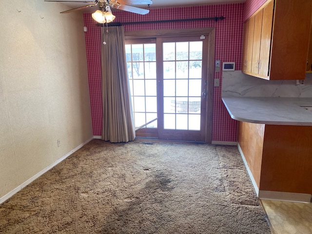 unfurnished dining area with baseboards, wallpapered walls, a ceiling fan, and light colored carpet