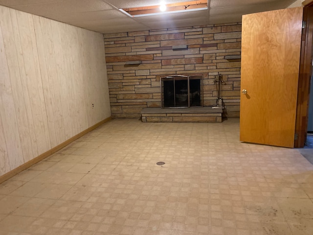 unfurnished living room with light floors, a drop ceiling, a fireplace, and wooden walls