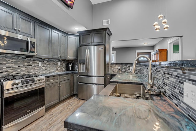 kitchen with a sink, visible vents, appliances with stainless steel finishes, light wood finished floors, and pendant lighting