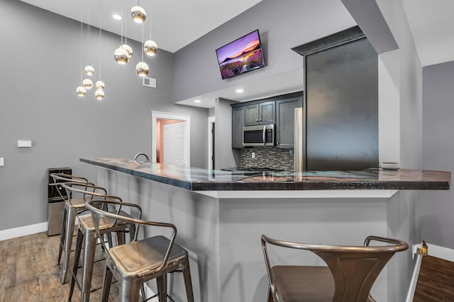 kitchen featuring hanging light fixtures, stainless steel microwave, a peninsula, and a breakfast bar area