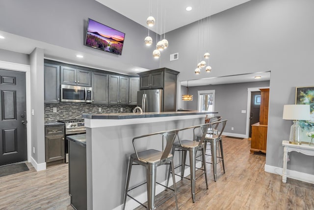 kitchen featuring a breakfast bar area, decorative light fixtures, appliances with stainless steel finishes, dark countertops, and a center island with sink