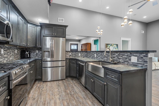 kitchen with pendant lighting, stainless steel appliances, visible vents, a sink, and wood finished floors