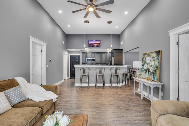 living room with recessed lighting, a towering ceiling, a ceiling fan, wood finished floors, and baseboards