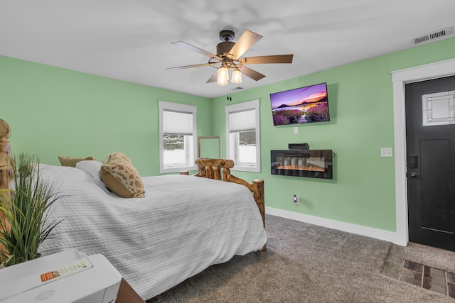 bedroom with carpet floors, visible vents, a glass covered fireplace, ceiling fan, and baseboards