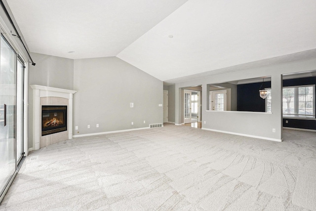 unfurnished living room with lofted ceiling, a tile fireplace, light carpet, visible vents, and baseboards