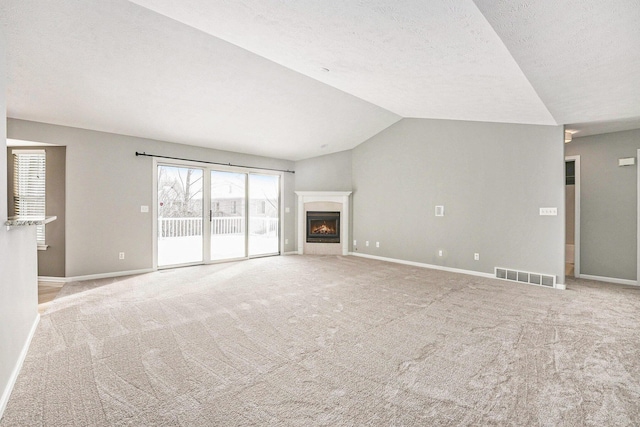 unfurnished living room featuring lofted ceiling, a lit fireplace, visible vents, and baseboards