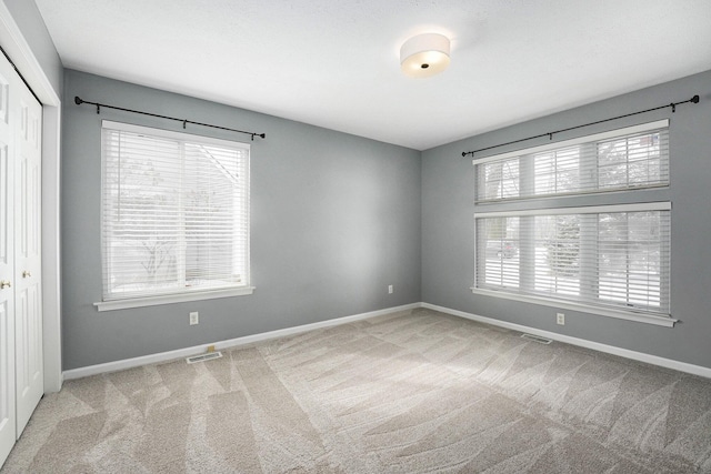 unfurnished room featuring visible vents, baseboards, and light colored carpet