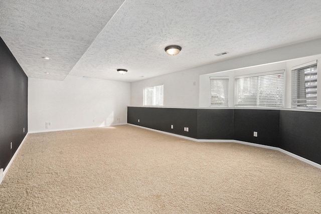 carpeted spare room with a textured ceiling, visible vents, and baseboards