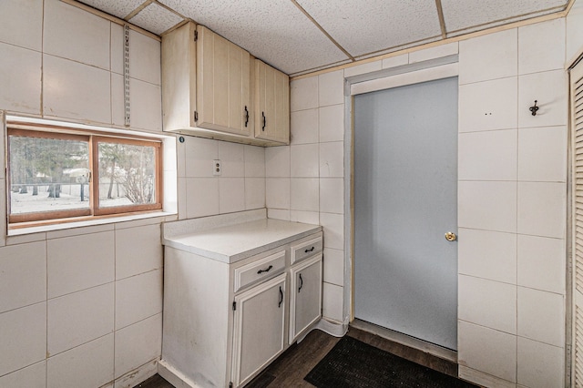 kitchen with dark wood-type flooring, tile walls, light countertops, and a drop ceiling