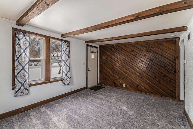 carpeted empty room featuring visible vents, wood walls, beam ceiling, and baseboards